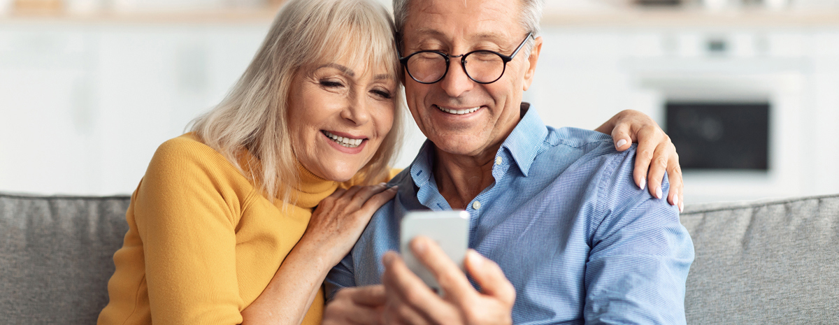 Par I Sofa Smiler Og Ser Paa Telefon
